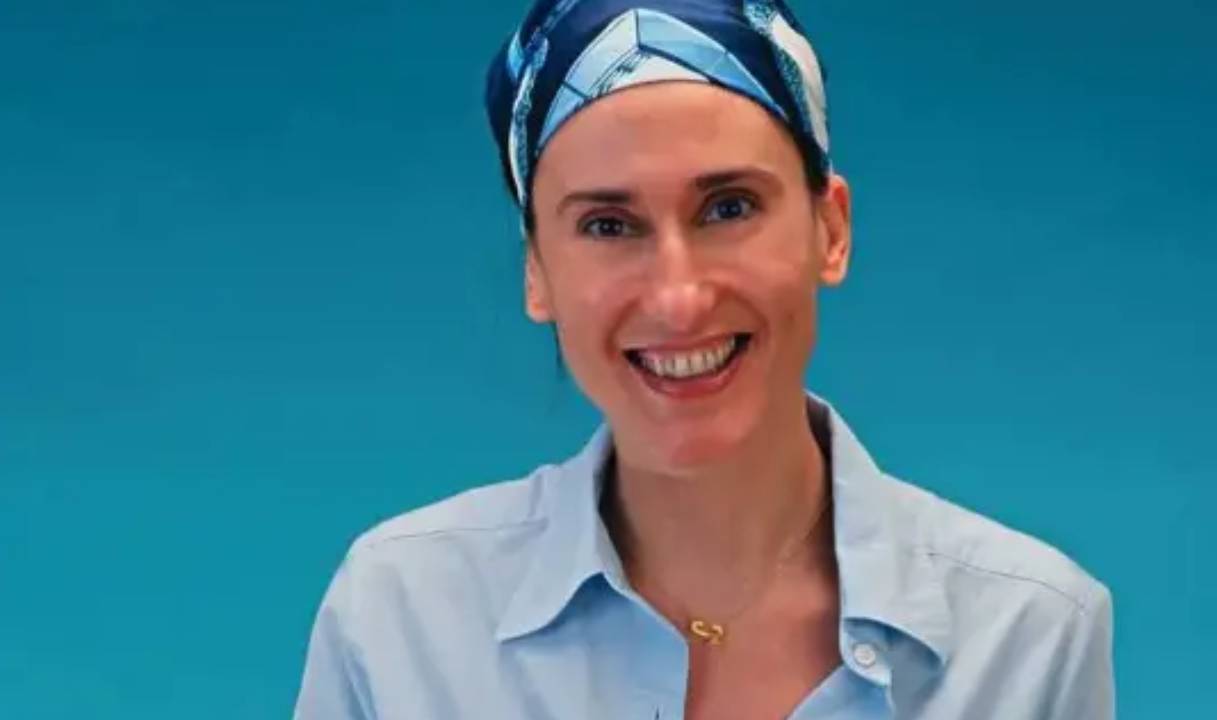 Em fundo azul, aparece um retrato da chef Paola Carosella de camisa azul e com um lenço azul na cabeça