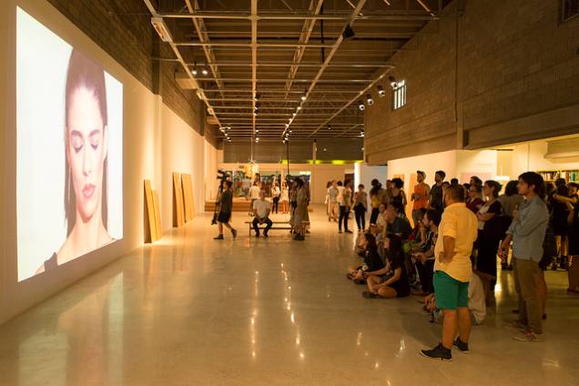 Público assiste um dos vídeos da exposição na noite de abertura do galpão