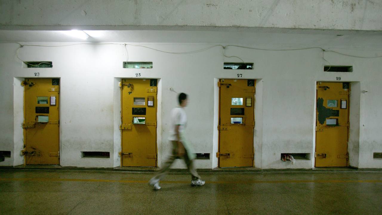 A imagem mostra um preso andando por corredores de uma penitenciária
