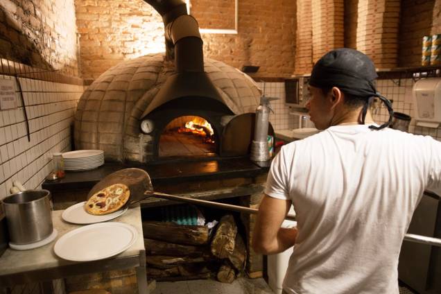 Num pequeno espaço, os pizzaiolos assam discos do tamanho de um prato Num pequeno espaço, os pizzaiolos assam discos do tamanho de um prato