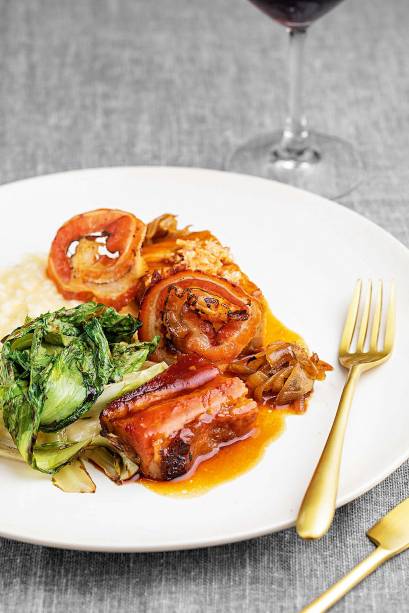 Barriga de porco em três versões: fresca e assada, curada e passada na grelha e defumada na forma de uma lâmina fina frita, como um bacon crocante, servida com risoto de parmesão, escarola tostada e cebola caramelizada