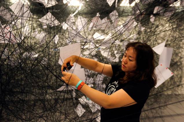 Chiharu Shiota montando a instalação <em>Cartas de Agradecimento, </em>que reúne 6000 cartas em uma teia de fios de lã