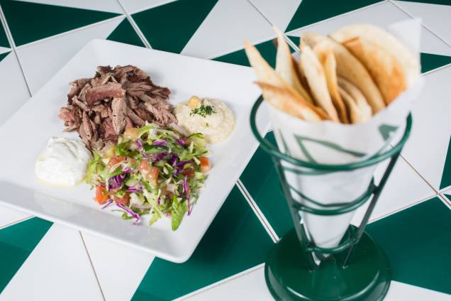 As lascas de chawarma chegam no prato, na companhia de salada, homus, coalhada seca e pão pita, servido à parte