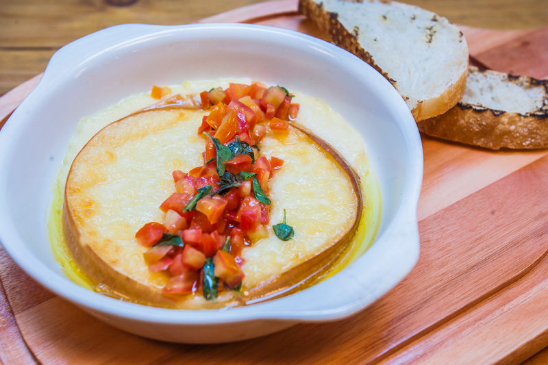 O provolone assado é acompanhado por cubos de tomate e molho de manjericão