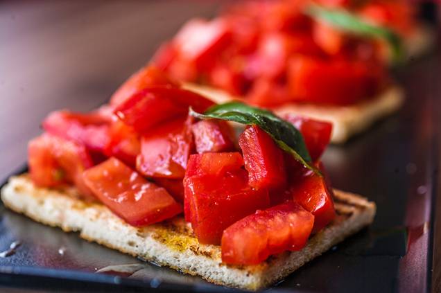 O trio de bruschettas com pedaços de tomate, folhas de manjericão e azeite