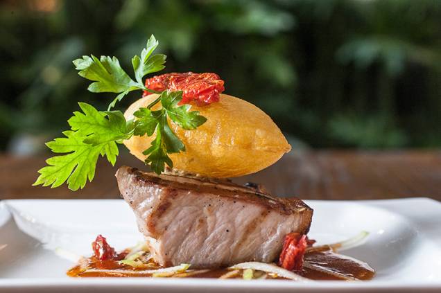 A picanha de porco vem rosada e com uma batata suflê sobre ela A picanha de porco vem rosada e com uma batata suflê sobre ela