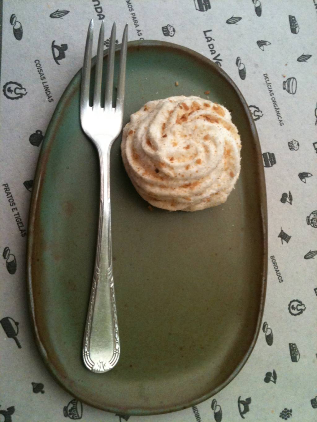 Taça de vidro com sorvete sobre base redonda de madeira, com pedaço de goiabada, pedaço de queijo e pequena faca ao lado, sobre mesa de madeira branca