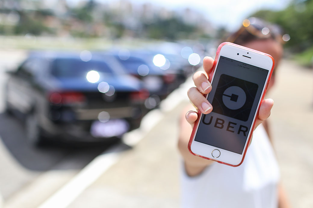 Foto mostra pessoa segurando celular com o logo da Uber