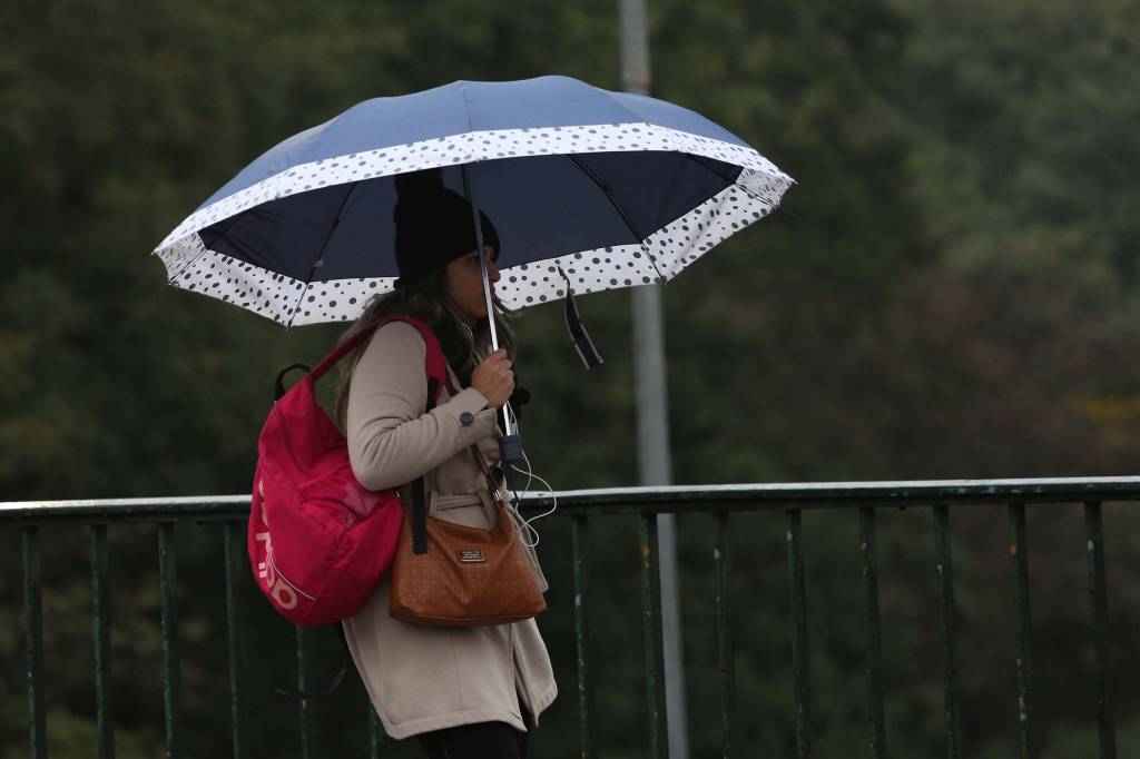 A imagem mostra uma mulher agasalhada e com guarda-chuva pelas ruas de São Paulo