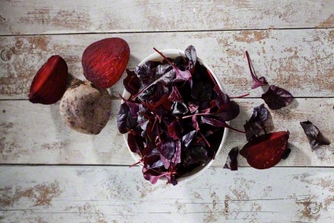 Beetroot and bowl of leaves on wood