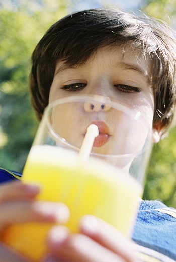 Boy drinking glass of orange juice with straw