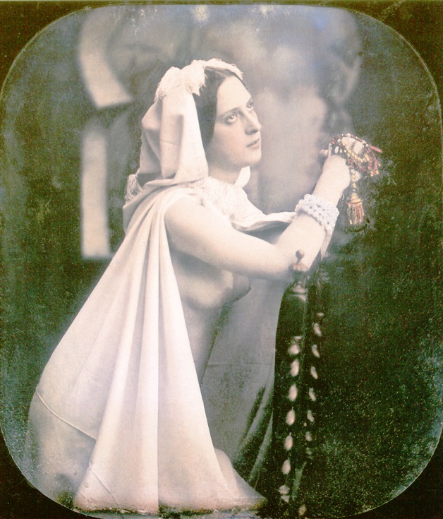 A woman is kneeling on a chair praying. 1850. She is wearing a white wedding dress which is open in the front showing her breasts. Hand-colored stereoscopic daguerreotype.   (Photo by Galerie Bilderwelt/Getty  Images)