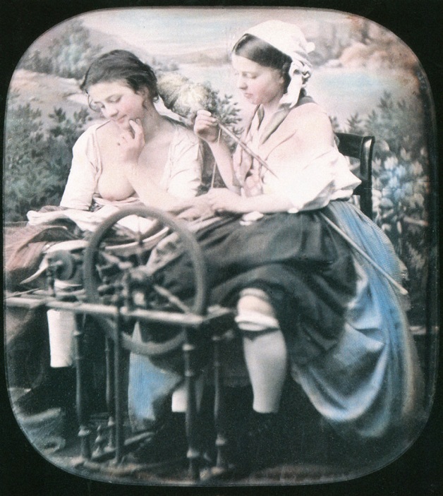 Two women are sitting next to another spinning in front of a studio curtain with countryside scenery.1850.One has her blouse unbuttonend and one of her breasts is showing. Hand-colored stereoscopic daguerreotype.   (Photo by Galerie Bilderwelt/Getty  Images)
