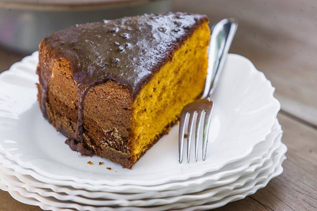 O bolo de cenoura é servido em fatia alta com cobertura de chocolate