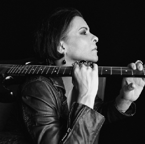 Foto em preto e branco mostra Marina Lima segurando uma guitarra na altura do ombro
