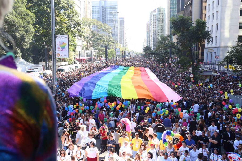 Imagem mostra multidão reunida na Avenida Paulista, com bandeira LGBT estendida
