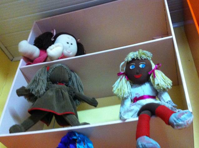 A boneca sem expressão (R$ 89,90) estimula a imaginação da criança. Ao lado, uma negra, com cabelo loiro (R$ 75,00). Na prateleira acima, uma boneca obesa (R$ 160,00)