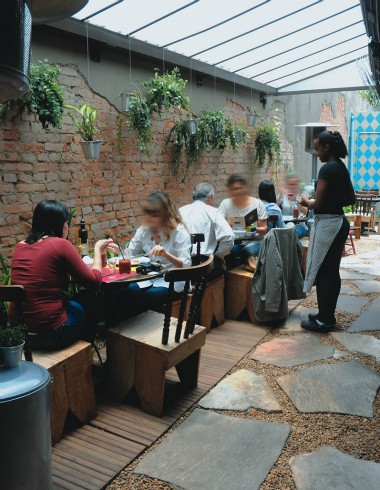 MEsas em jardim com atendente em pé e clientes sentados