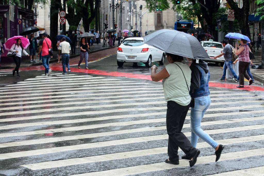 Imagem mostra pessoas em guarda-chuvas andando na rua
