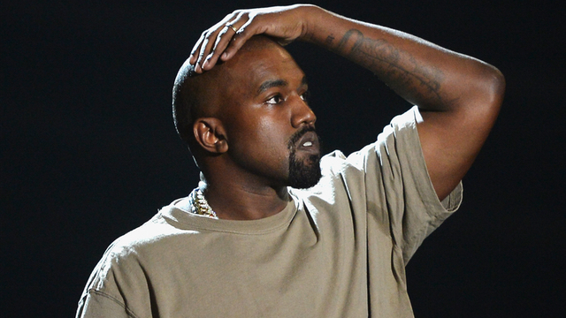 Imagem mostra Kanye West usando camiseta. Ele coloca a mão na cabeça e olha para a esquerda