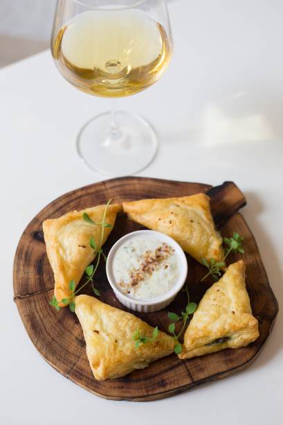 Espanacopita: torta de espinafre vem como um pastelzinho assado, triangular, recheado de queijo feta e crocante de azeitona junto de tzatziki, o pepino em iogurte e alho