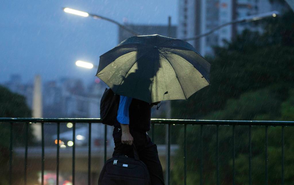 Imagem mostra pedestre caminhando com guarda-chuva