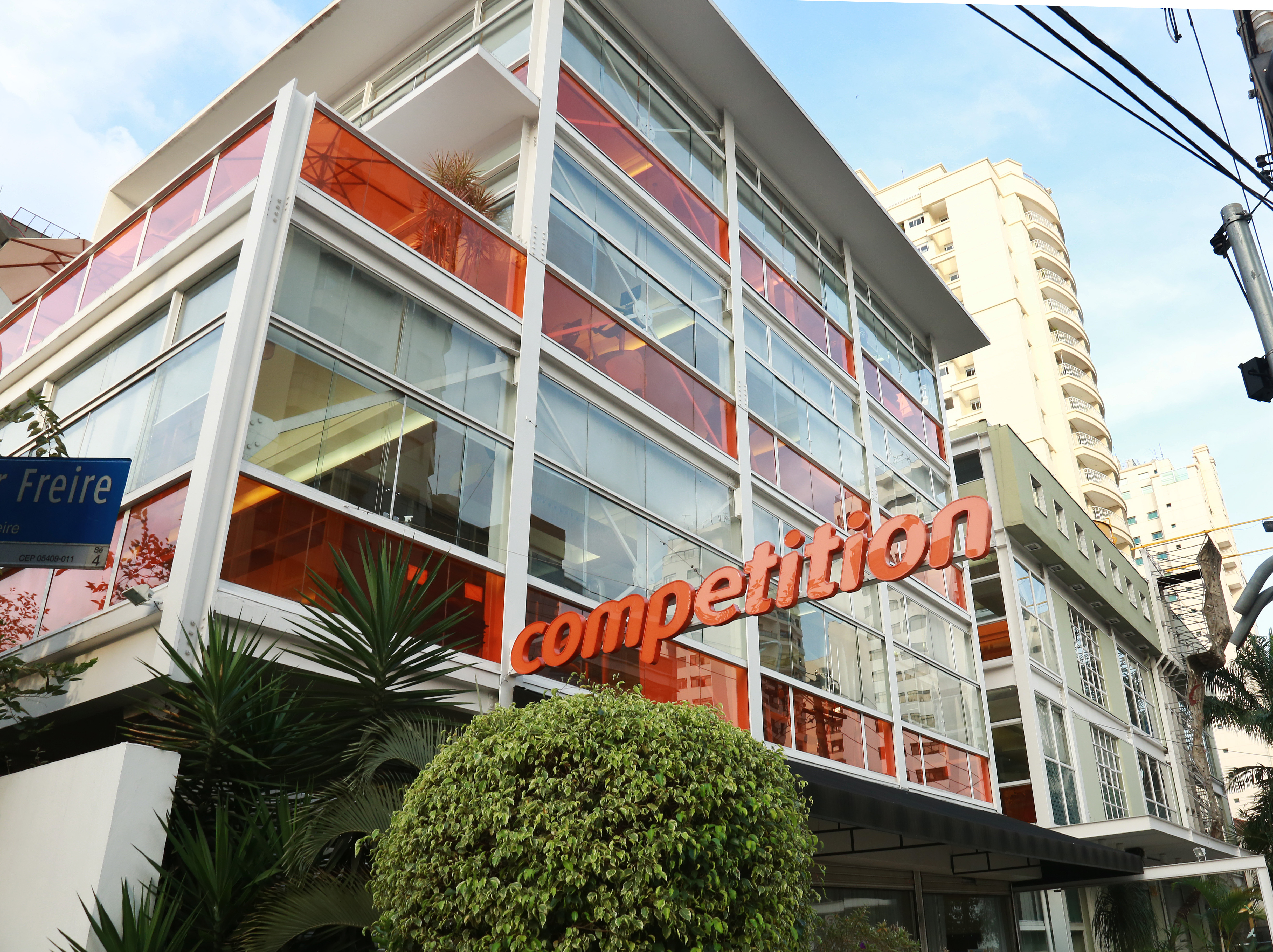 Imagem mostra um prédio com vidros transparentes e laranjas e uma placa escrita "competition"