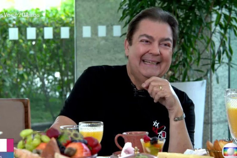 Imagem mostra Faustão sorrindo diante de mesa de café da manhã repleta de frutas e sucos