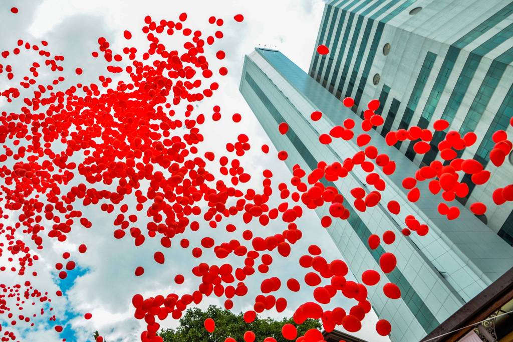 Imagem mostra dezenas de balões vermelhos subindo em direção ao céu ao lado de prédio do Hospital das Clínicas da USP