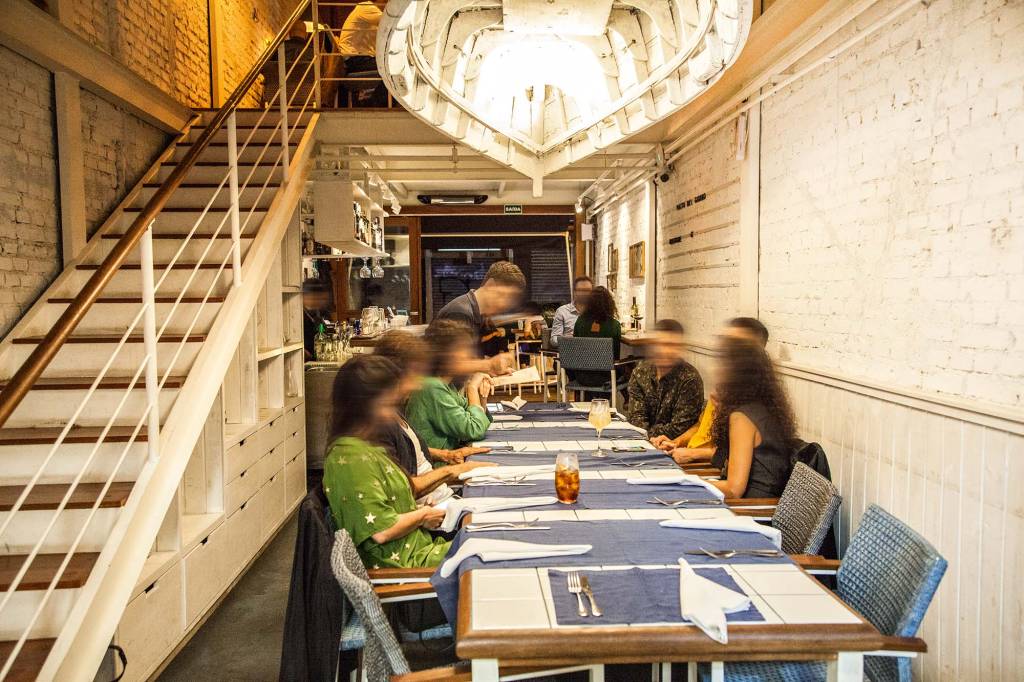 Parte térrea do salão do restaurante Lido Amici di Amici com pessoas sentadas em uma mesa coletiva