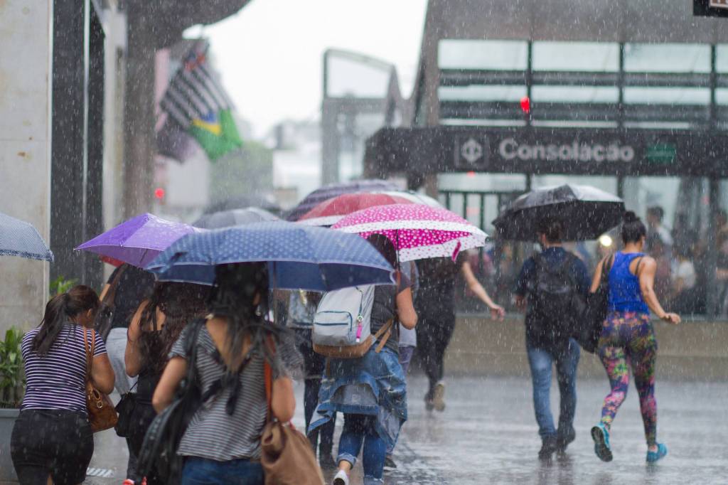 Imagem mostra pedestres caminhando na Avenida Paulista, próximo do metrô Consolação, embaixo de chuva