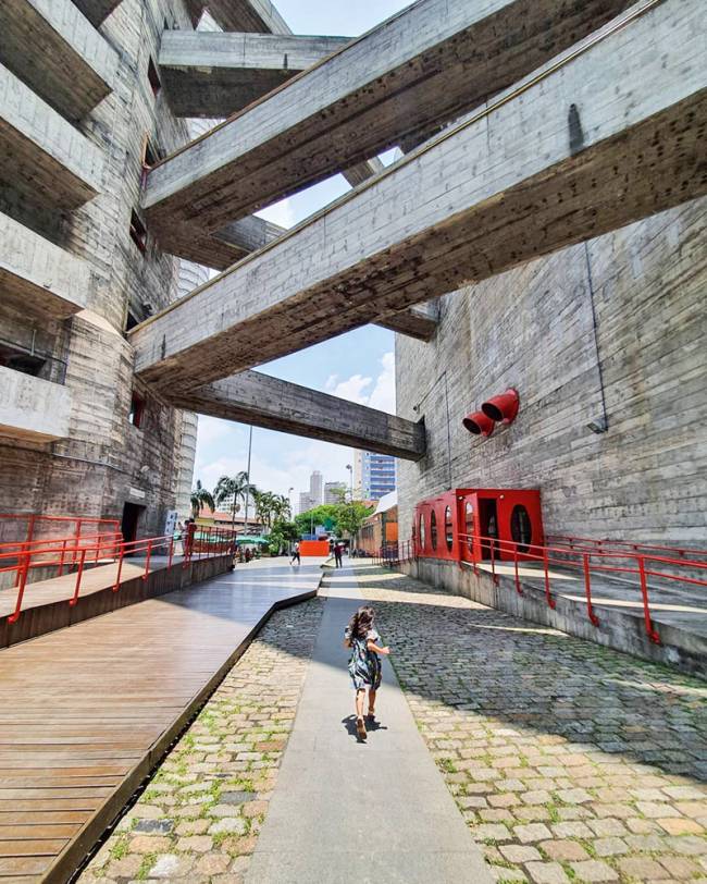 materia instagram leitores conexões suspensas entre os prédios do sesc pompeia. espaço entre eles é amplo e de passagem, tem uma menina andando