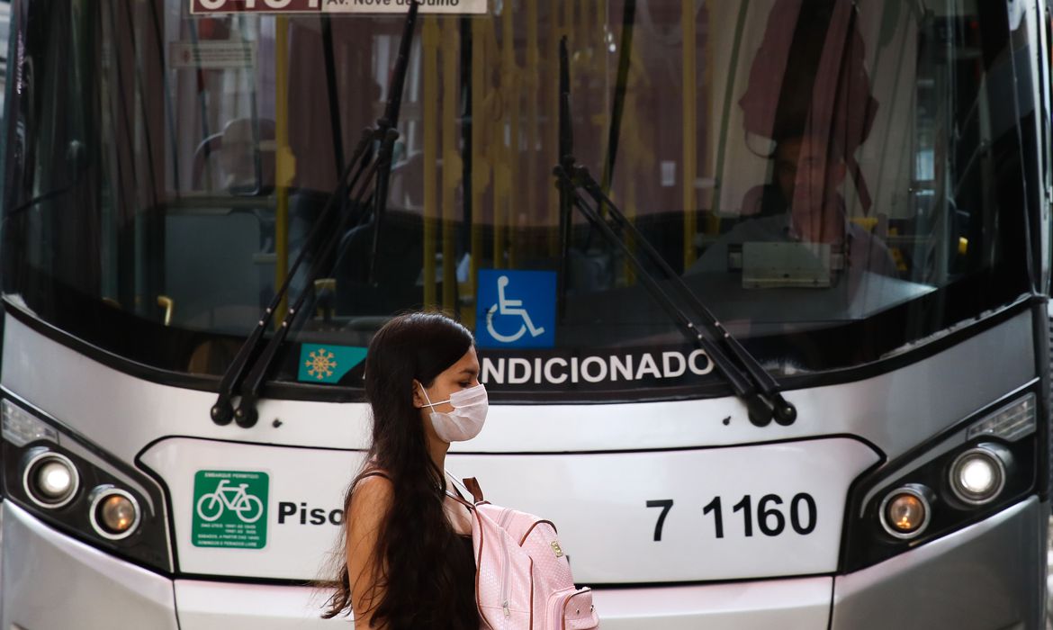 Imagem mostra mulher de máscara na frente de ônibus municipal