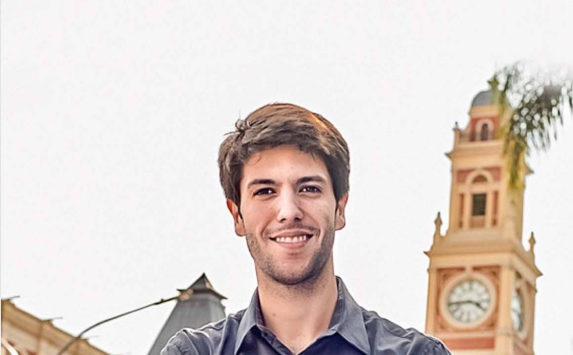 Imagem mostra Caio, com camisa polo, na frente da Estação da Luz