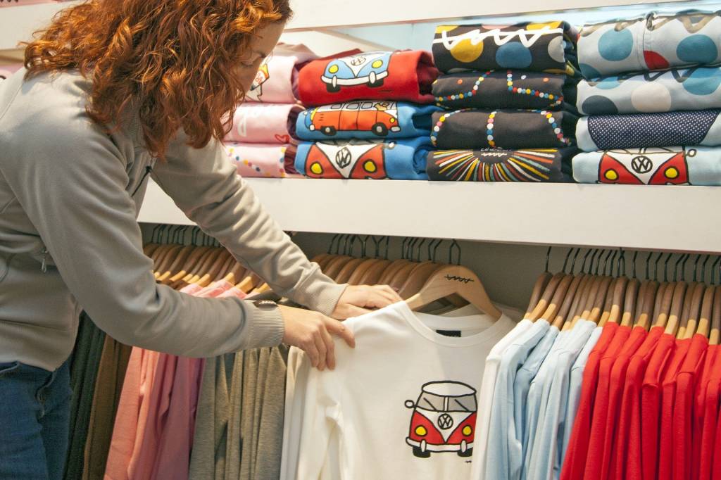 Mulher olha camiseta em cabideiro em loja de roupas