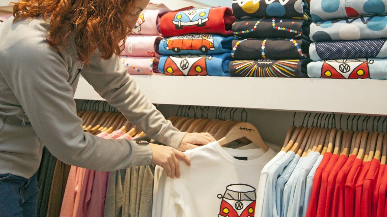 Mulher olha camiseta em cabideiro em loja de roupas