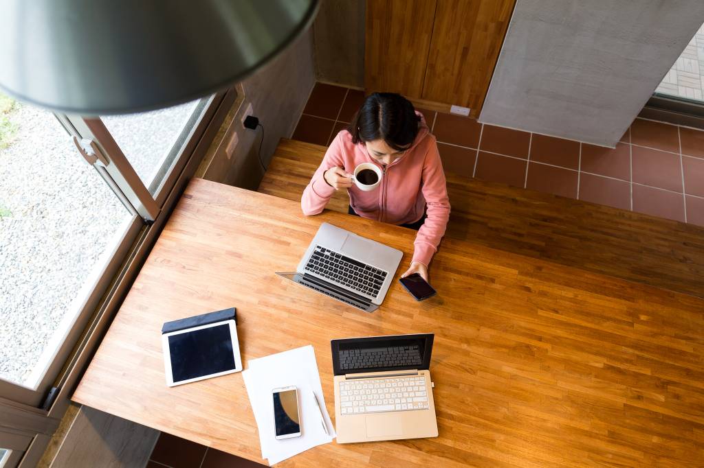 Imagem mostra mulher sentada em mesa diante de computador, trabalhando em regime de home office