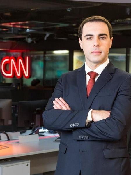 A imagem mostra Rafael Colombo, com os braços cruzados e de terno, encarando a câmera. Ao fundo, há o logo da CNN.