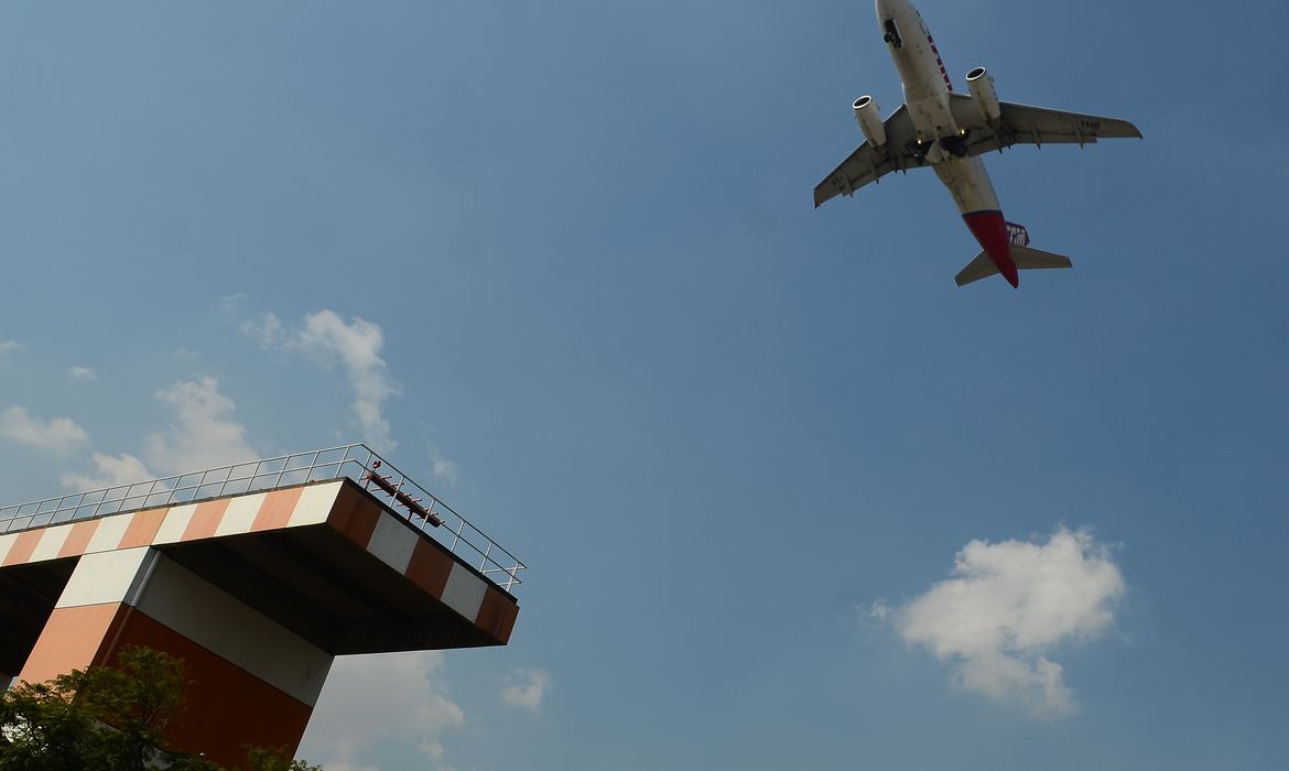 Imagem mostra avião visto de baixo e torre de controle aéreo no Aeroporto de Congonhas.