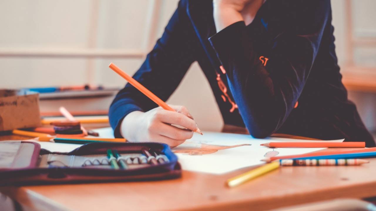 A imagem mostra uma criança debruçada sobre uma mesa com lápis na mão