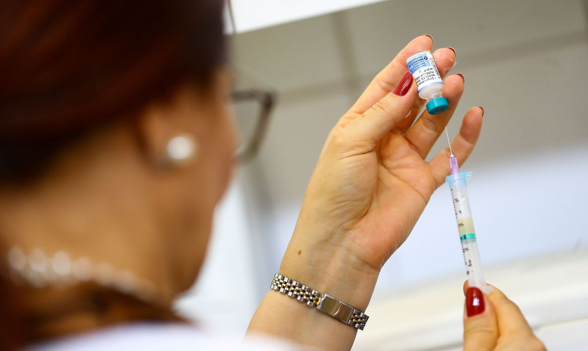 Imagem mostra mulher retirando dose de vacina de frasco com seringa