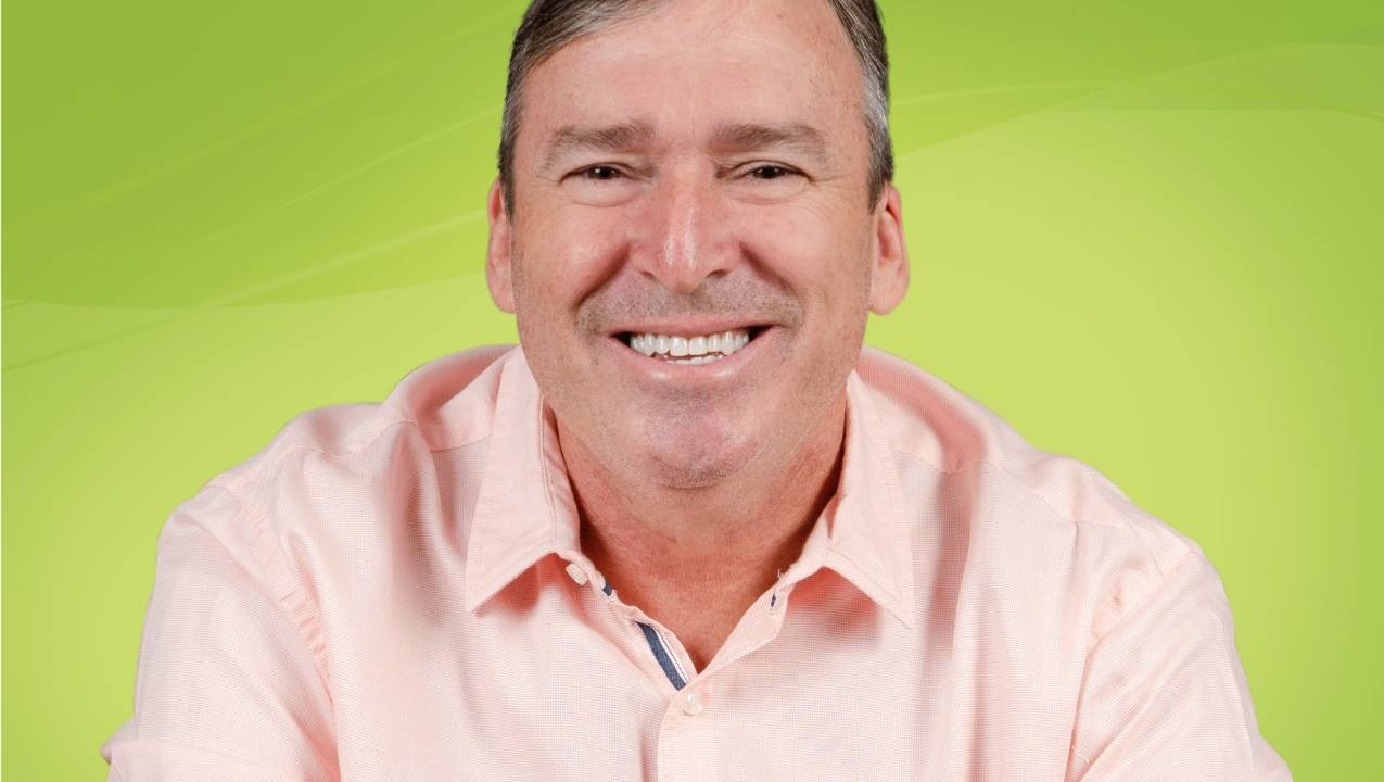 Adriano Moreno sorrindo com camisa rosa e fundo verde