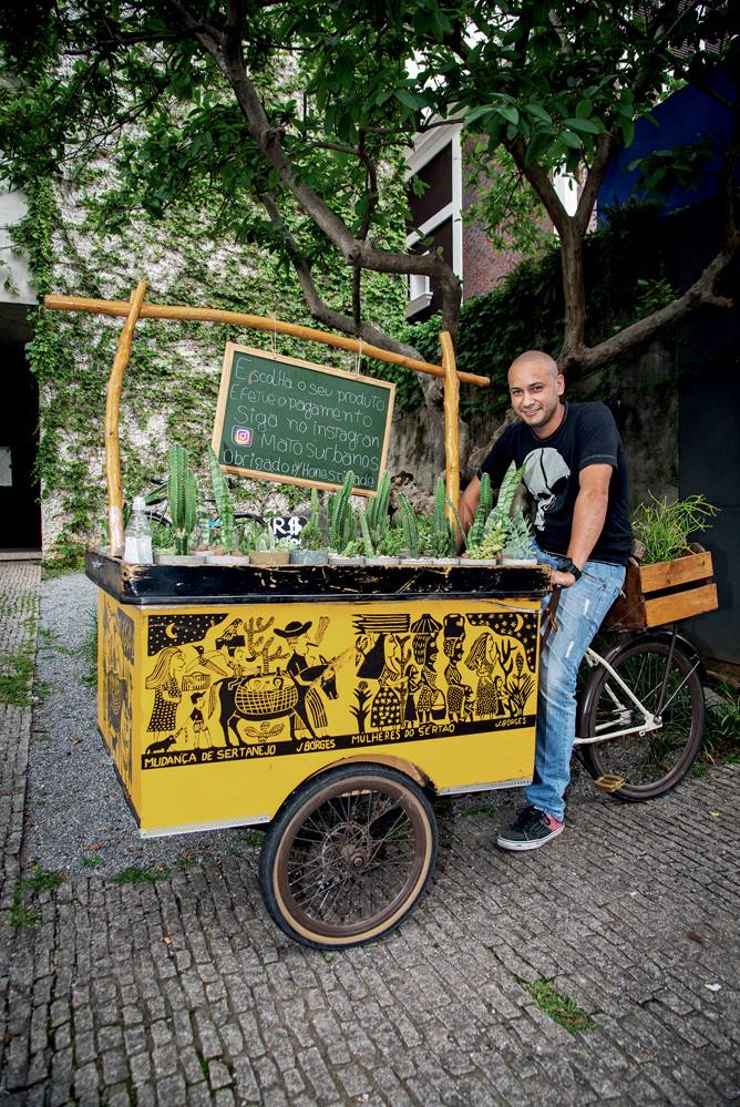 Israel Joaquim posa sentado em bicicleta com bancada amarela, mini-lousa com nome 