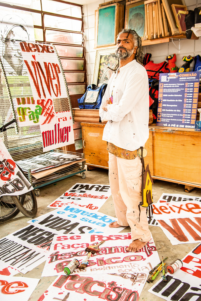 Mauro Neri, em pé, com diversos cartazes escritos com mensagens antiracistas e contra violência