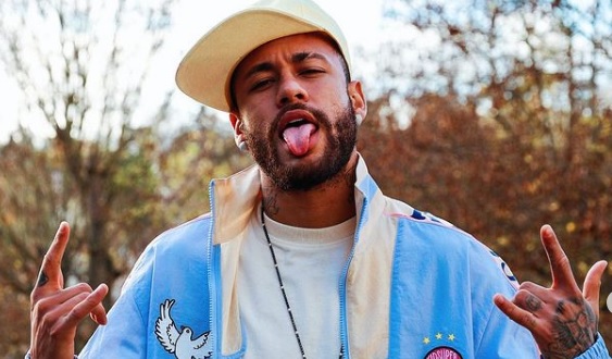 Neymar, jogador do Paris Saint-German, aparece com boné ranco, jaqueta azul e a língua para fora da boca