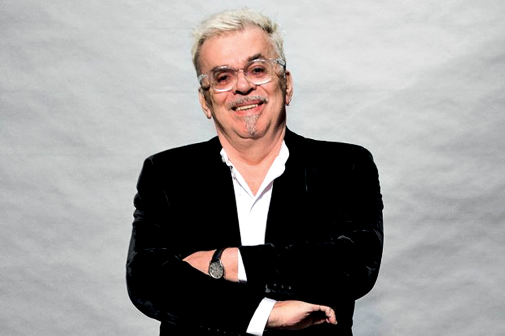 Autor Walcyr Carrasco posa de braços cruzados com terno preto, camisa branca, relógio, óculos transparentes e cabelos grisalhos.