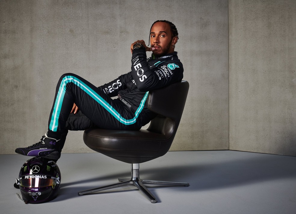 Lewis Hamilton posando em cima de uma cadeira com os pés sobre um capacete