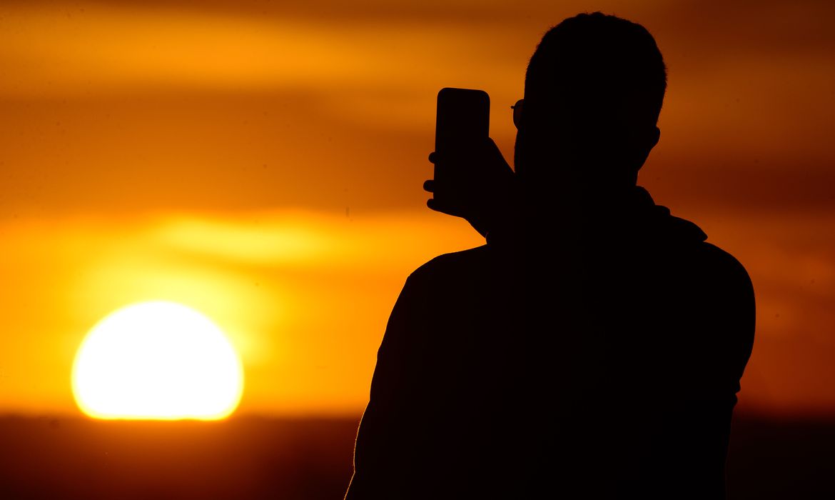 Imagem mostra homem fotografando pôr do sol