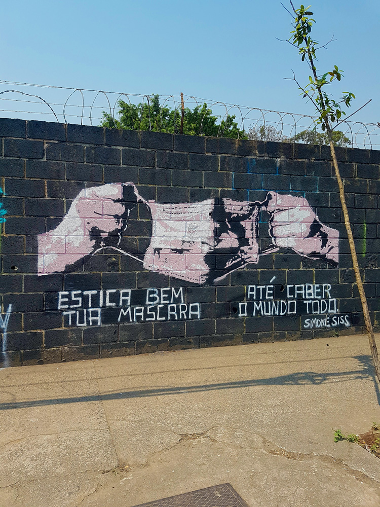 Mural em que duas mão mantém uma máscara estendida. Em baixo da imagem está escrito 