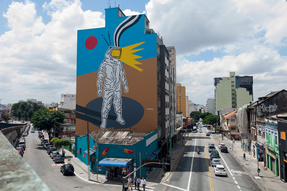 Mural feito em um prédio. Um astronauta com cabeça de televisão.